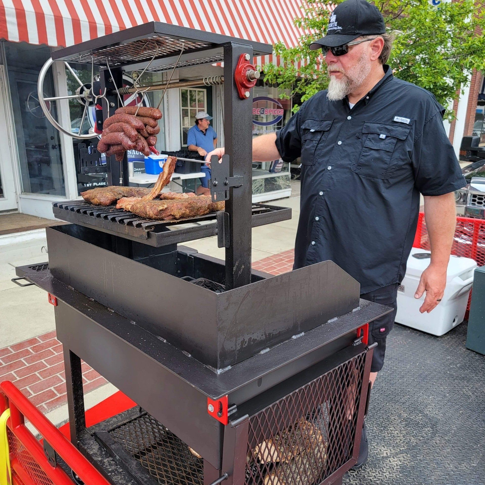 A man in a black shirt is cooking meat on a grill