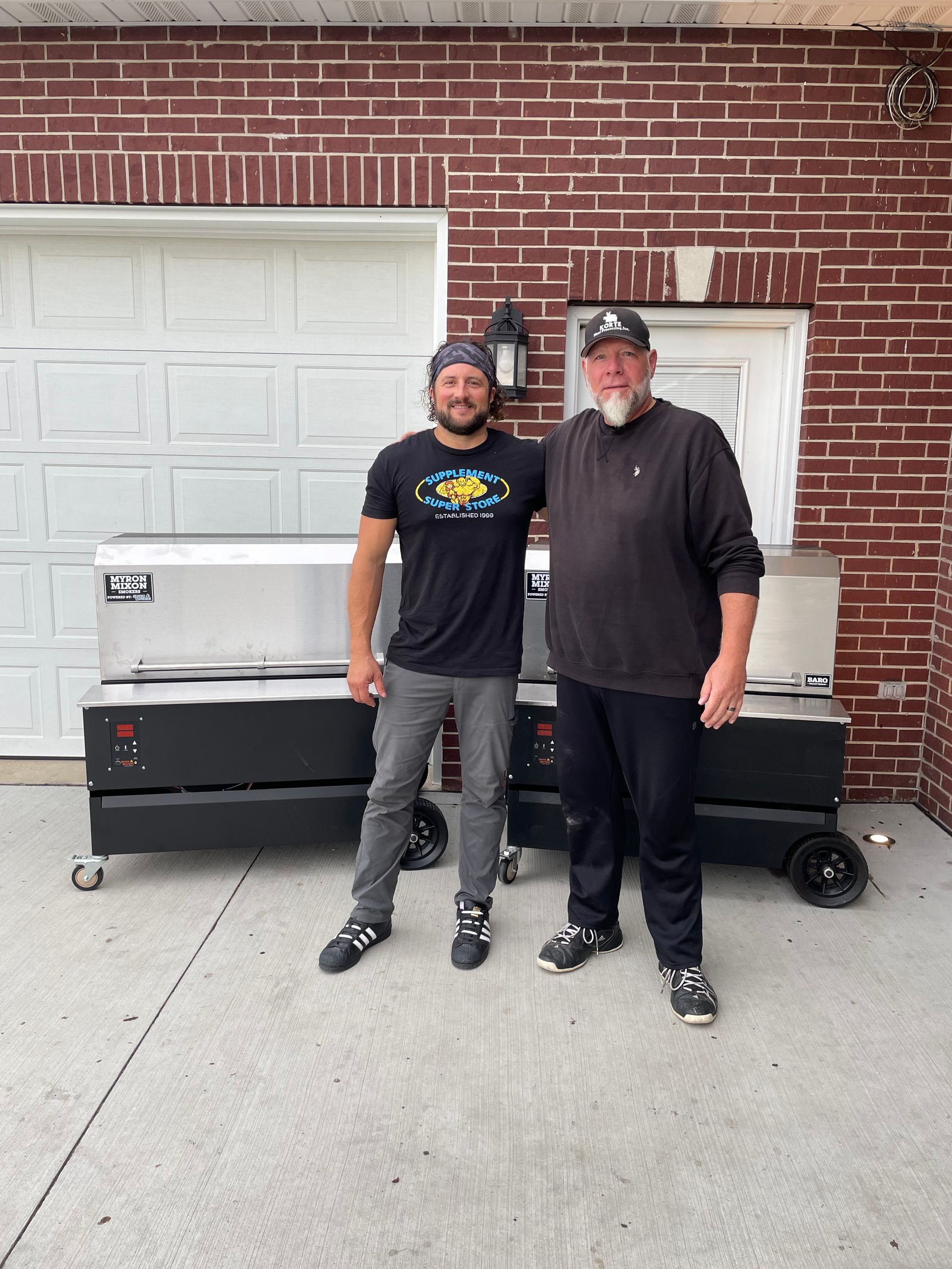 Two men are standing next to each other in front of a brick building.