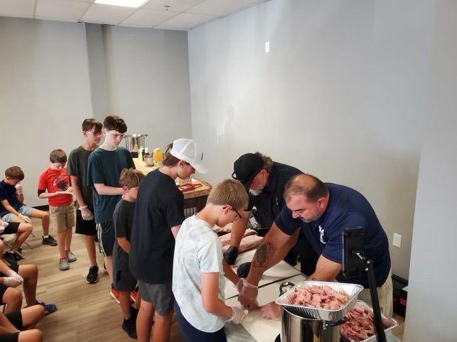 A group of people are standing around a table with meat on it.