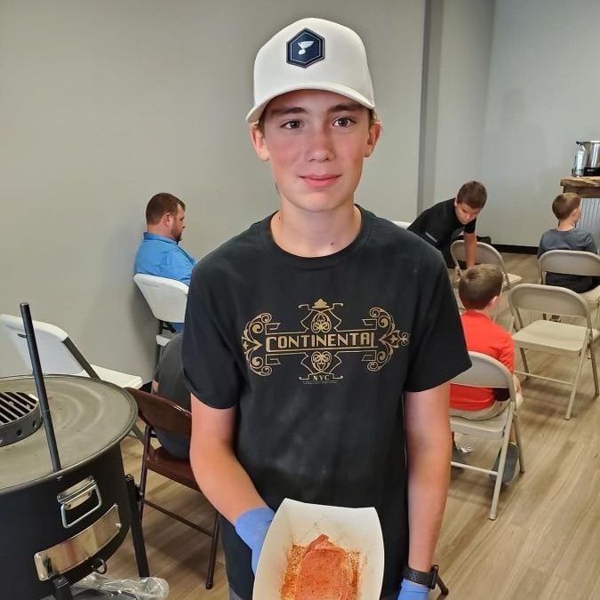 A young boy wearing a black shirt that says continental is holding a piece of food