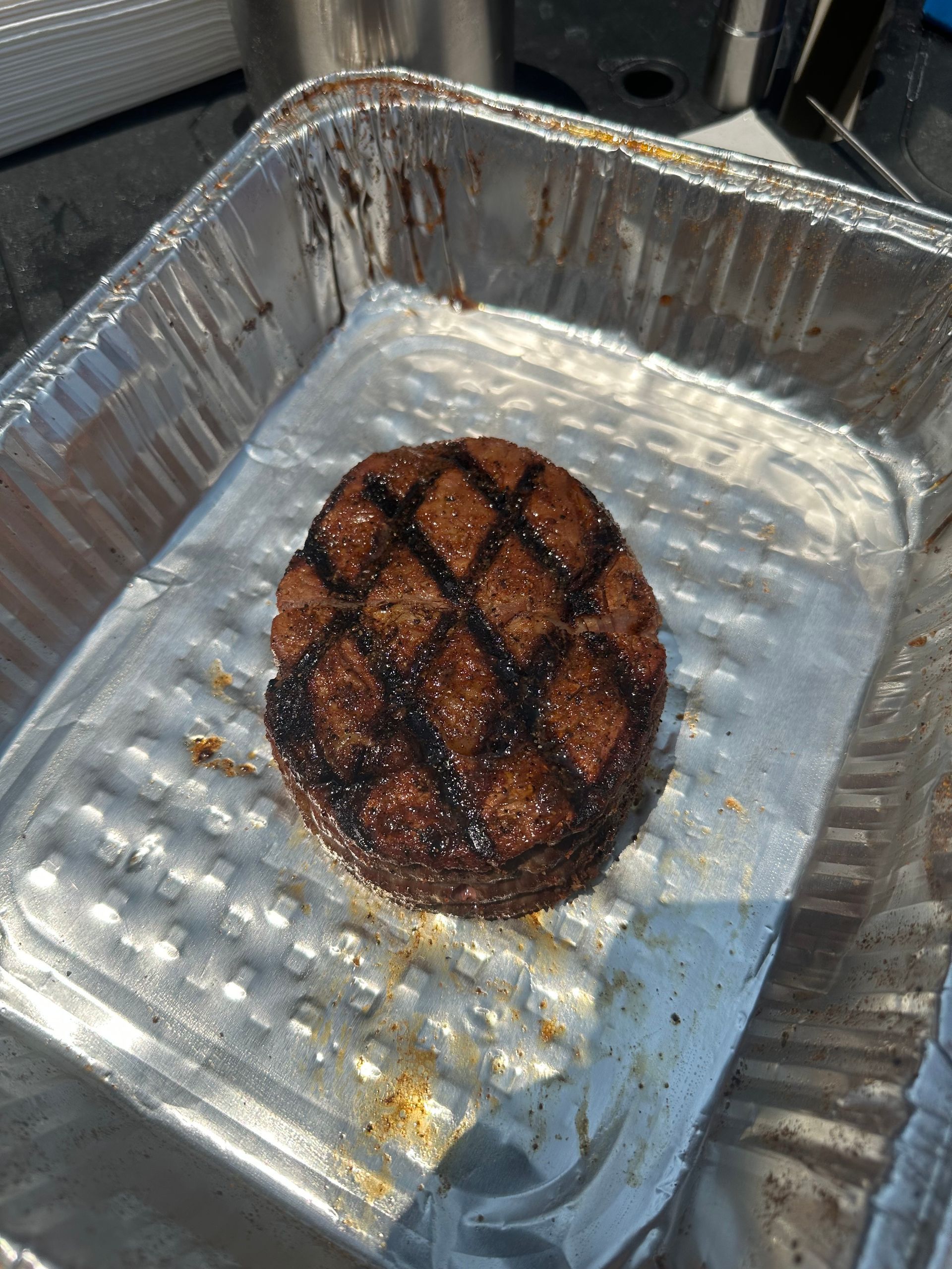 A hamburger patty is sitting in a tin foil pan.