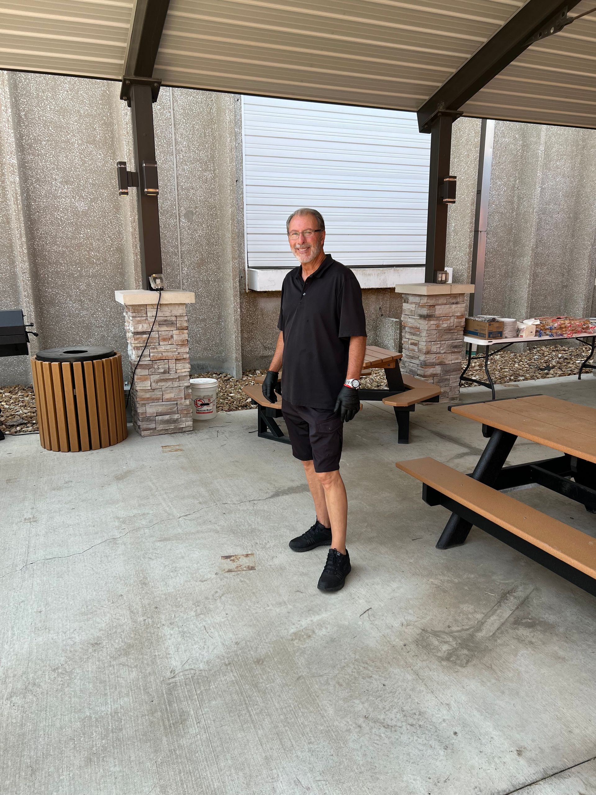 A man in a black shirt is standing in front of a picnic table.