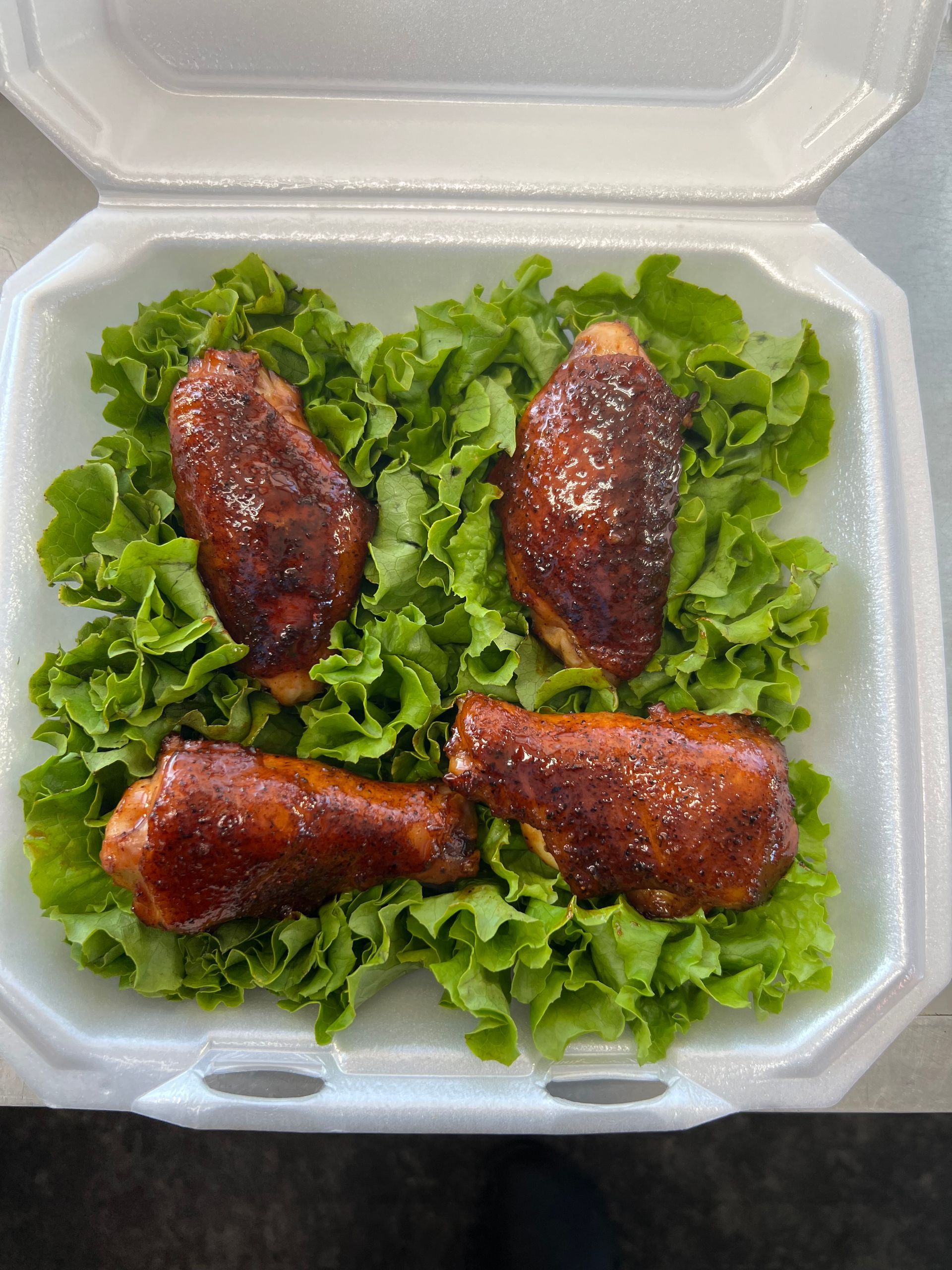 A styrofoam container filled with chicken wings and lettuce.