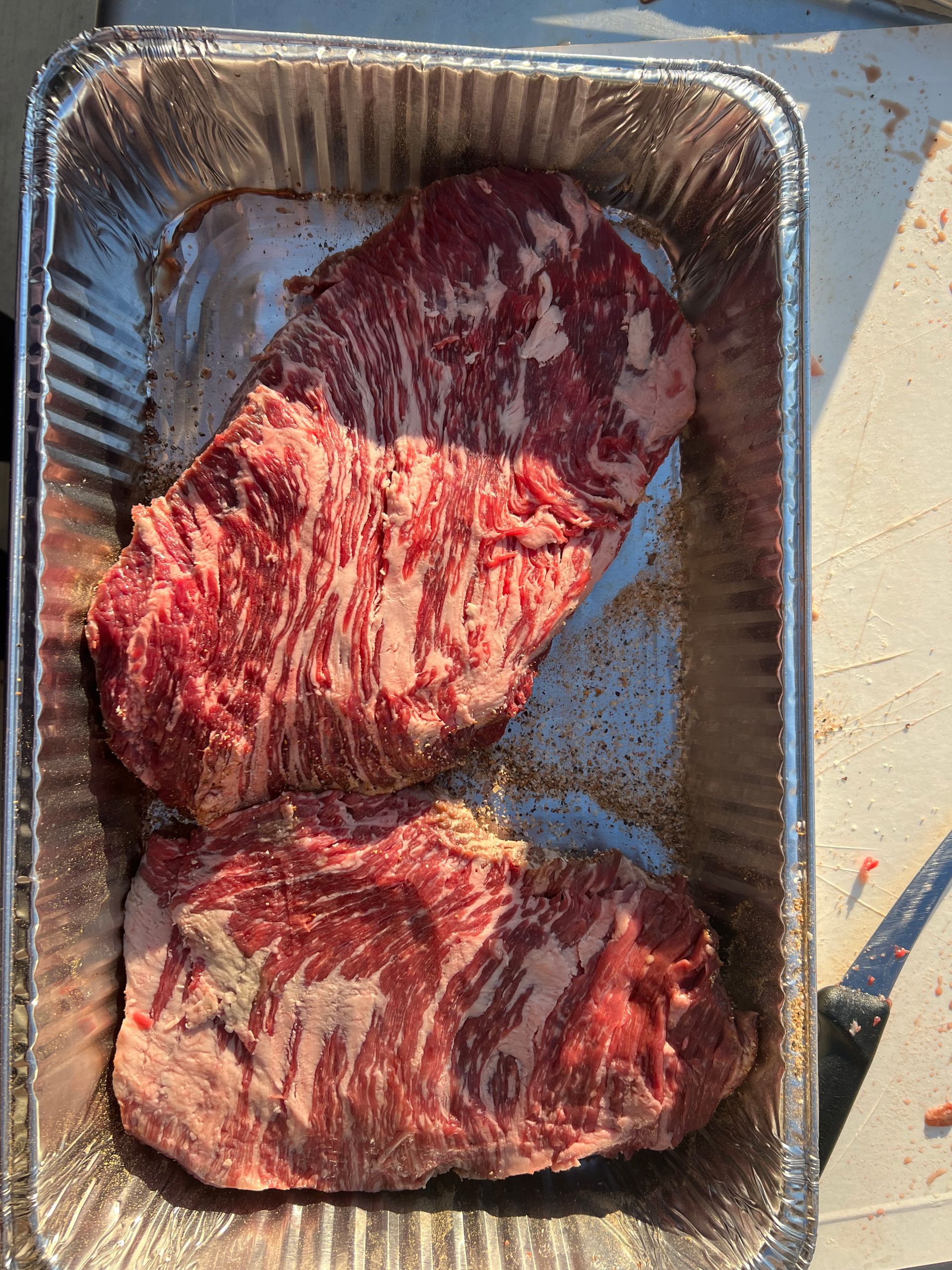 Two pieces of raw beef are in a tin foil pan.