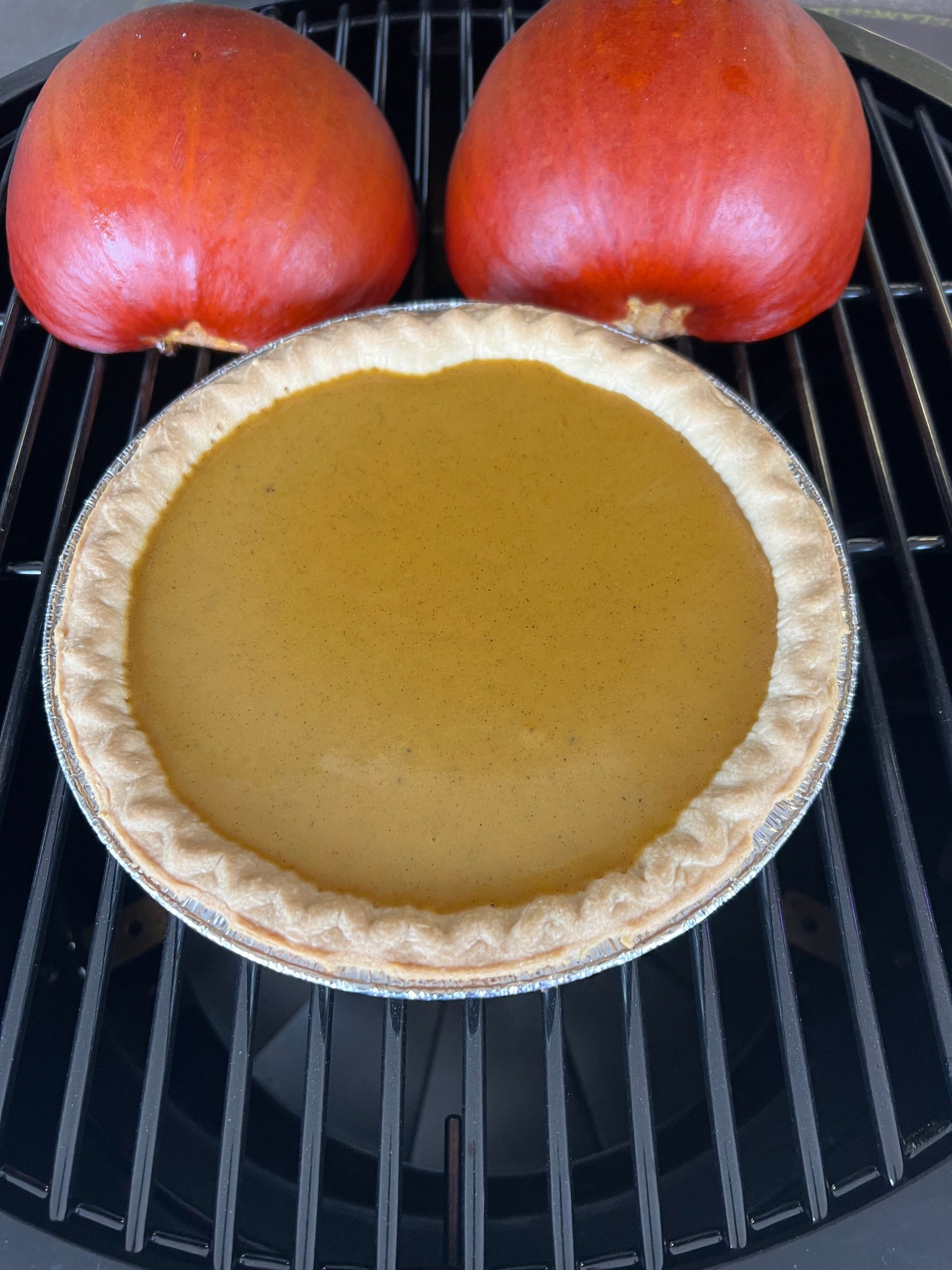 A pie is sitting on a grill next to two pumpkins