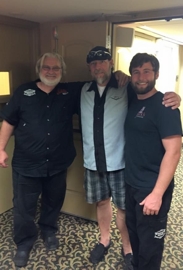 Three men posing for a picture with one wearing a harley davidson shirt