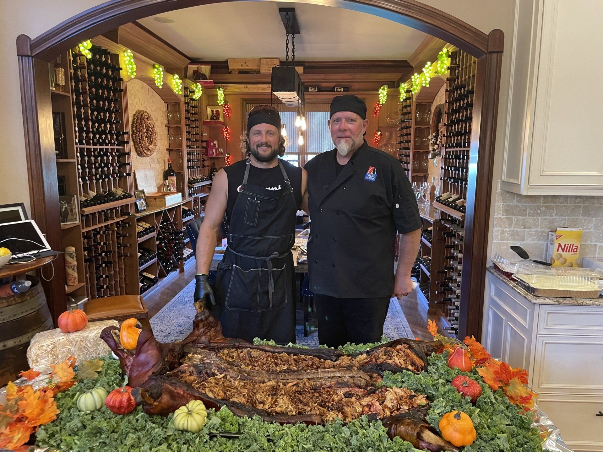 Two men are standing next to a large tray of food in a kitchen.