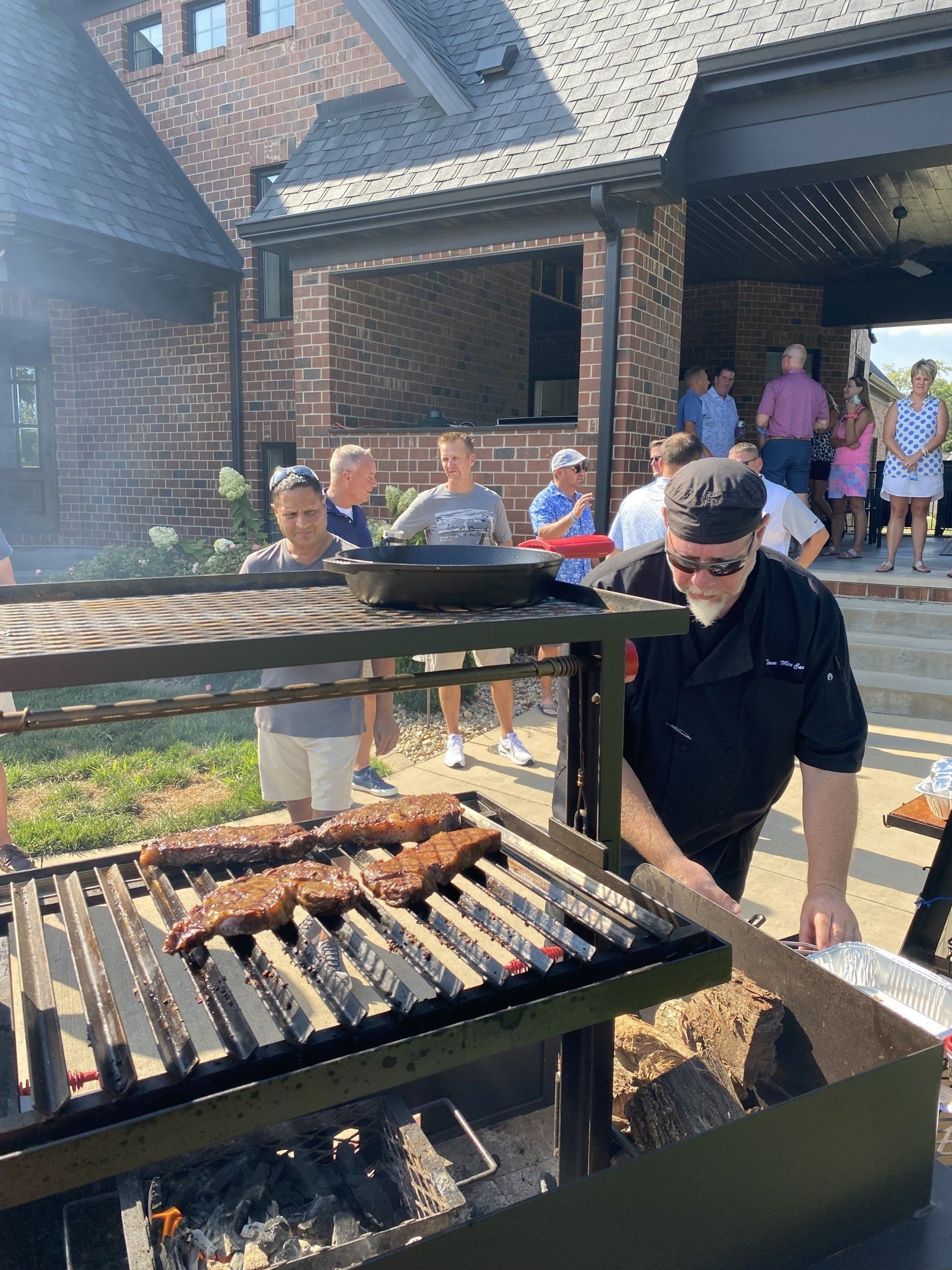 A man is cooking meat on a grill in front of a group of people.