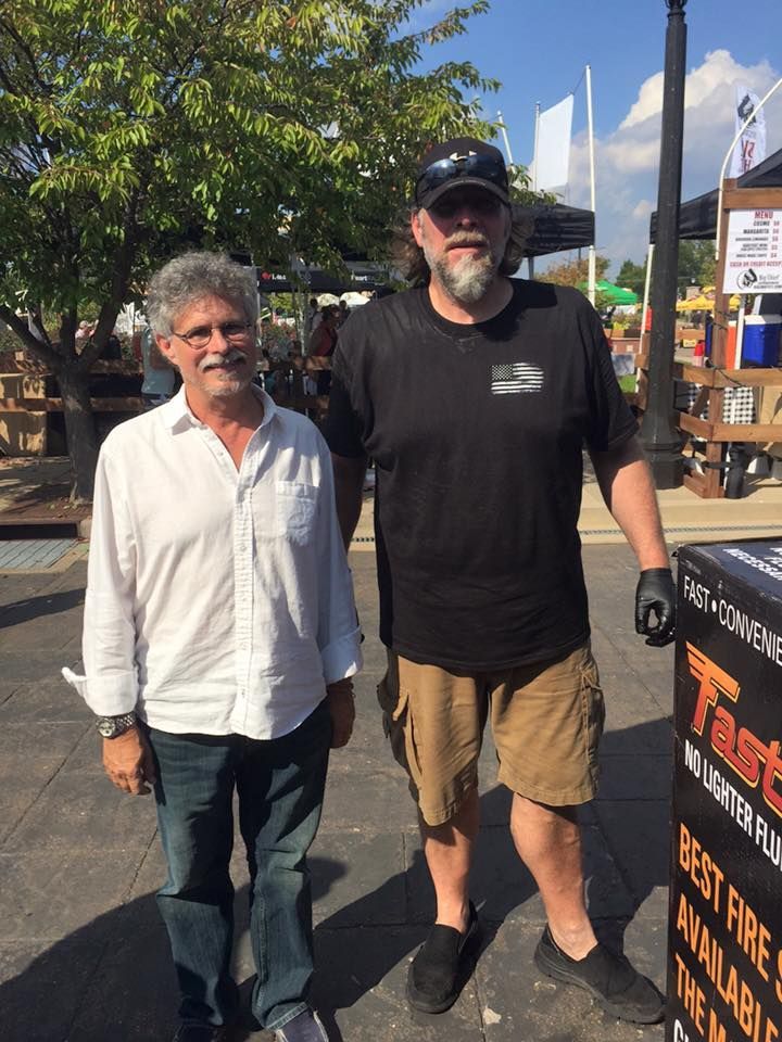 Two men are standing next to each other in front of a sign that says best fire available