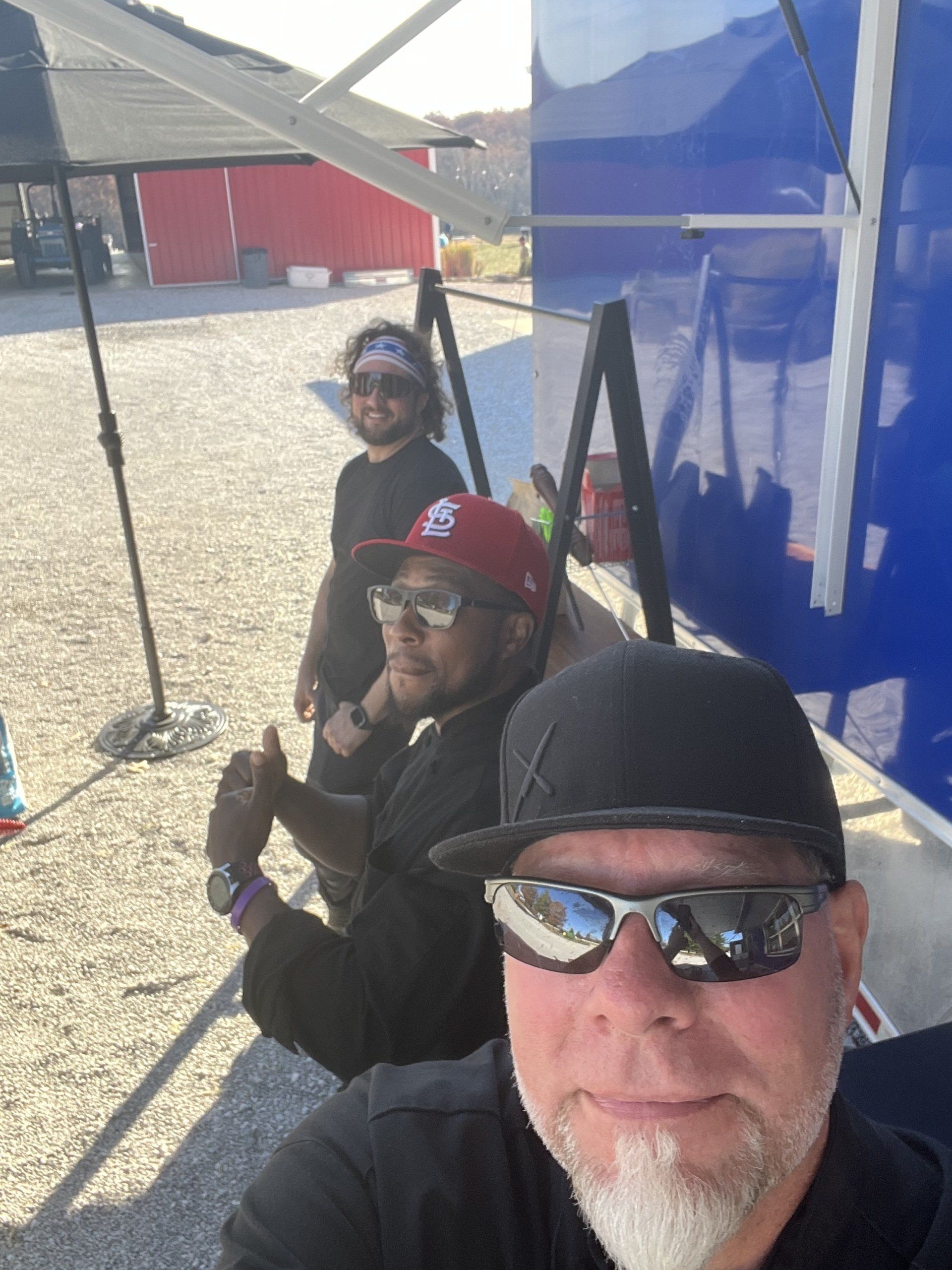 A man wearing sunglasses and a hat is sitting next to two other men