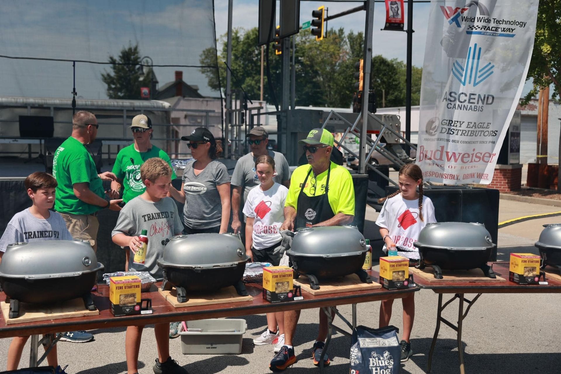 A group of people are standing around a table with grills.