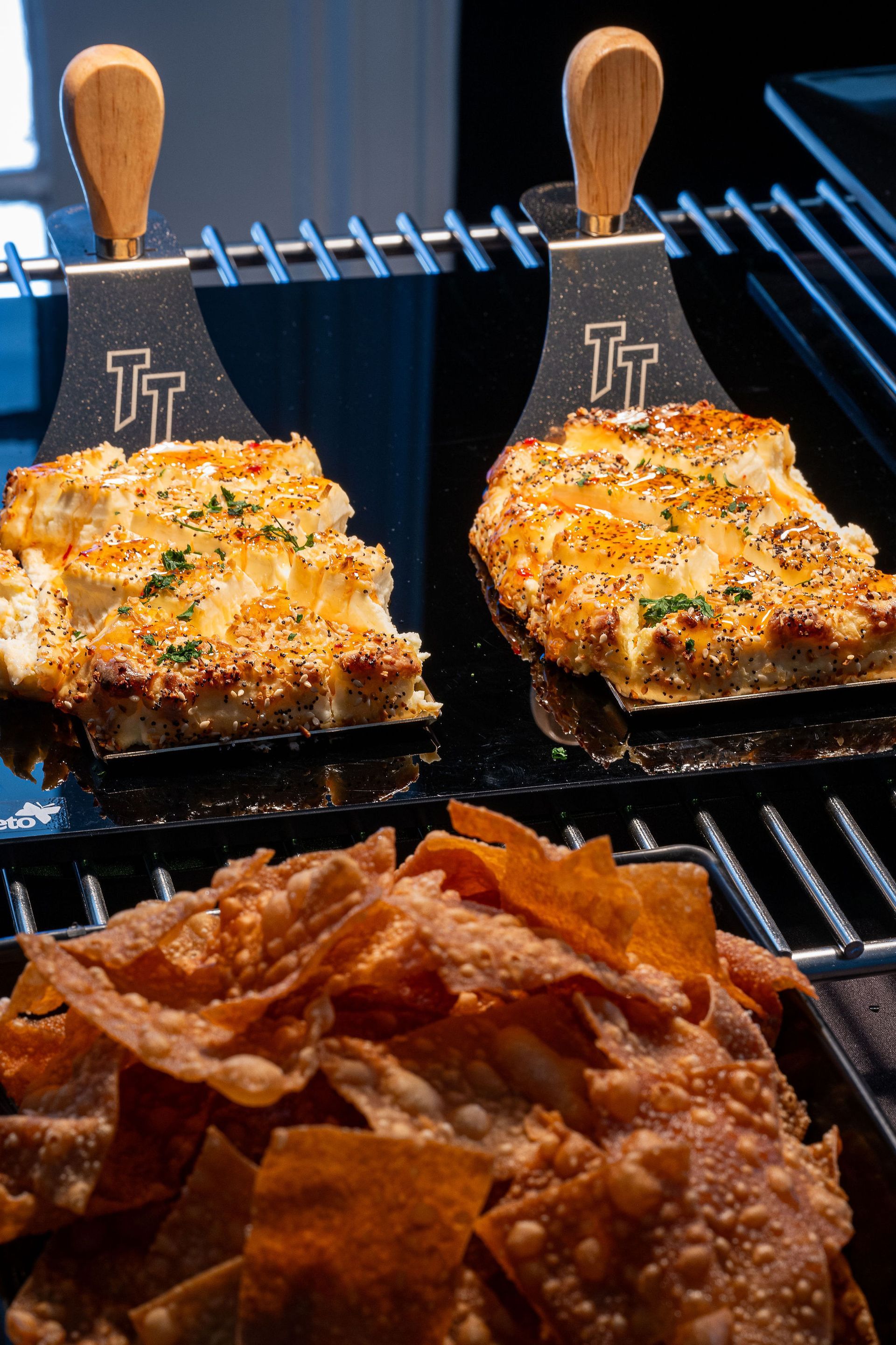 Two pieces of food are sitting on a grill next to a bowl of chips.