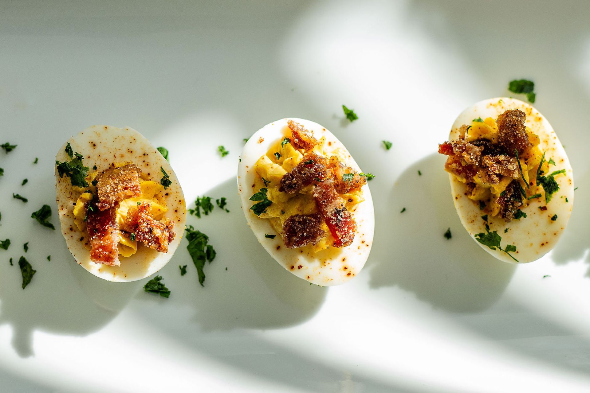 Three hard boiled eggs with bacon and parsley on a white plate.