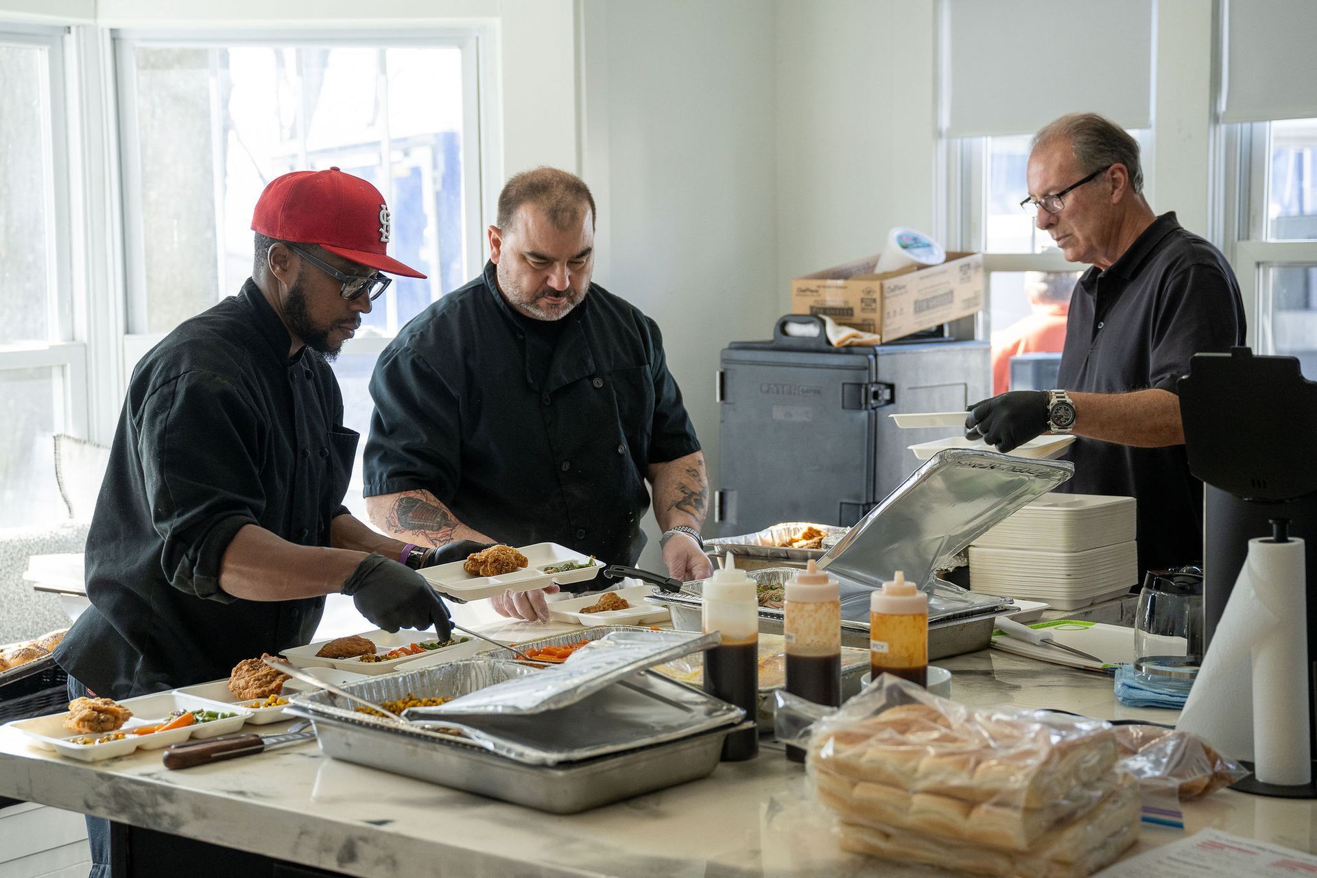 Three men are preparing food on a table in a kitchen.