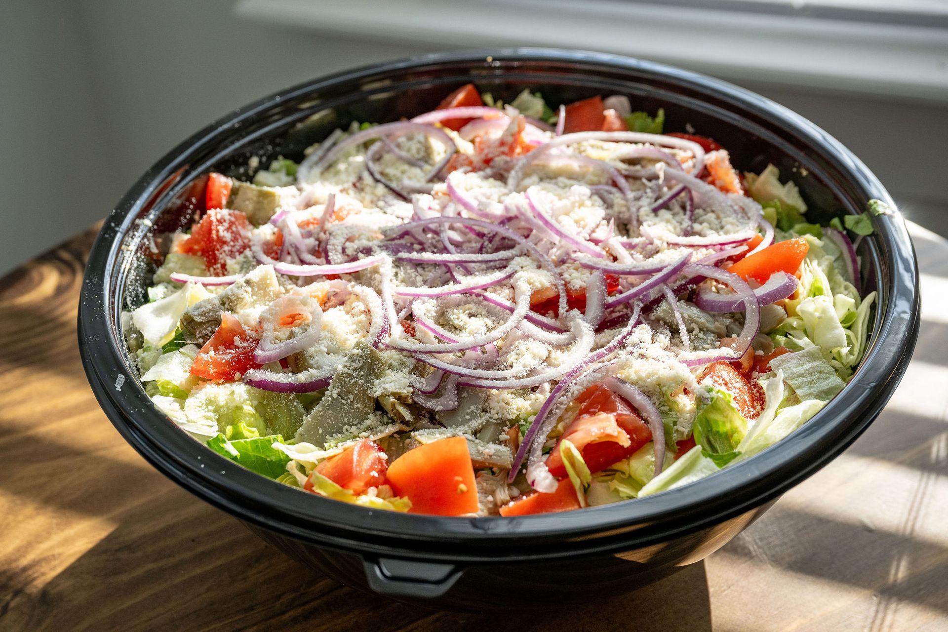 A bowl of salad with tomatoes , lettuce , onions and cheese on a wooden table.