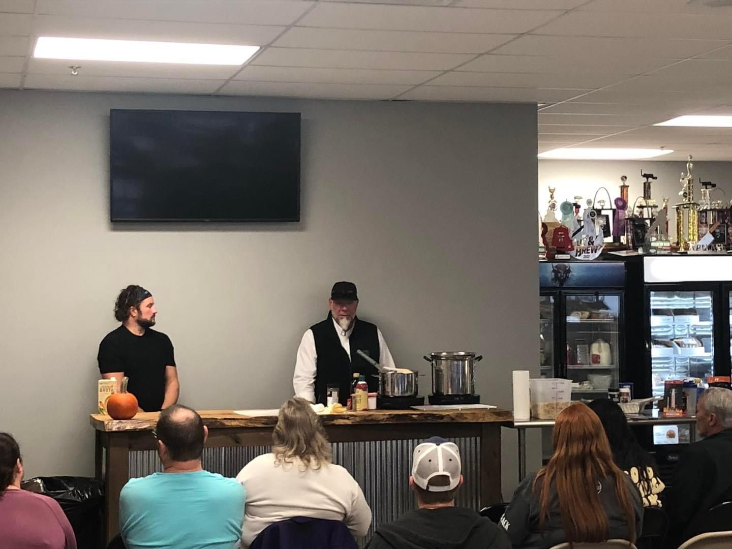 A group of people are sitting in a room watching a man cooking.