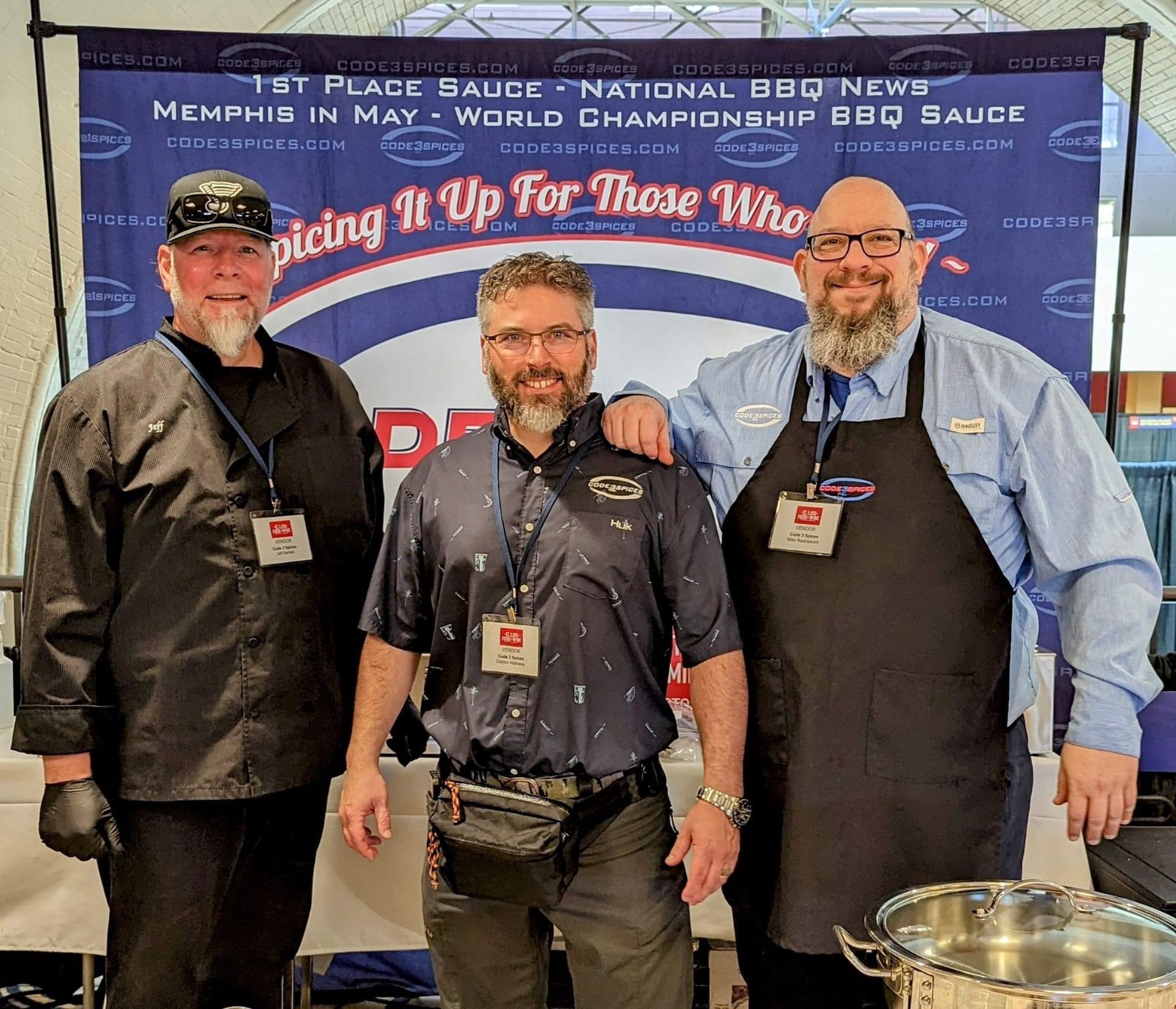 Three men standing in front of a sign that says spicing it up for those who