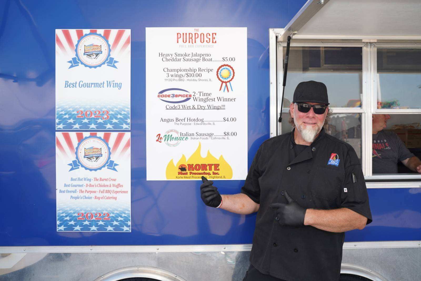 A man is standing in front of a food truck holding a sign.