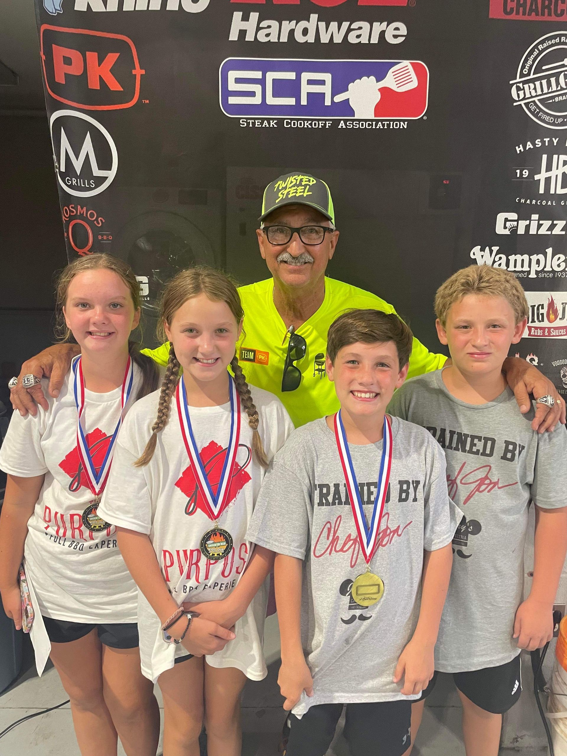 A group of children are posing for a picture with a man in front of a hardware sign.