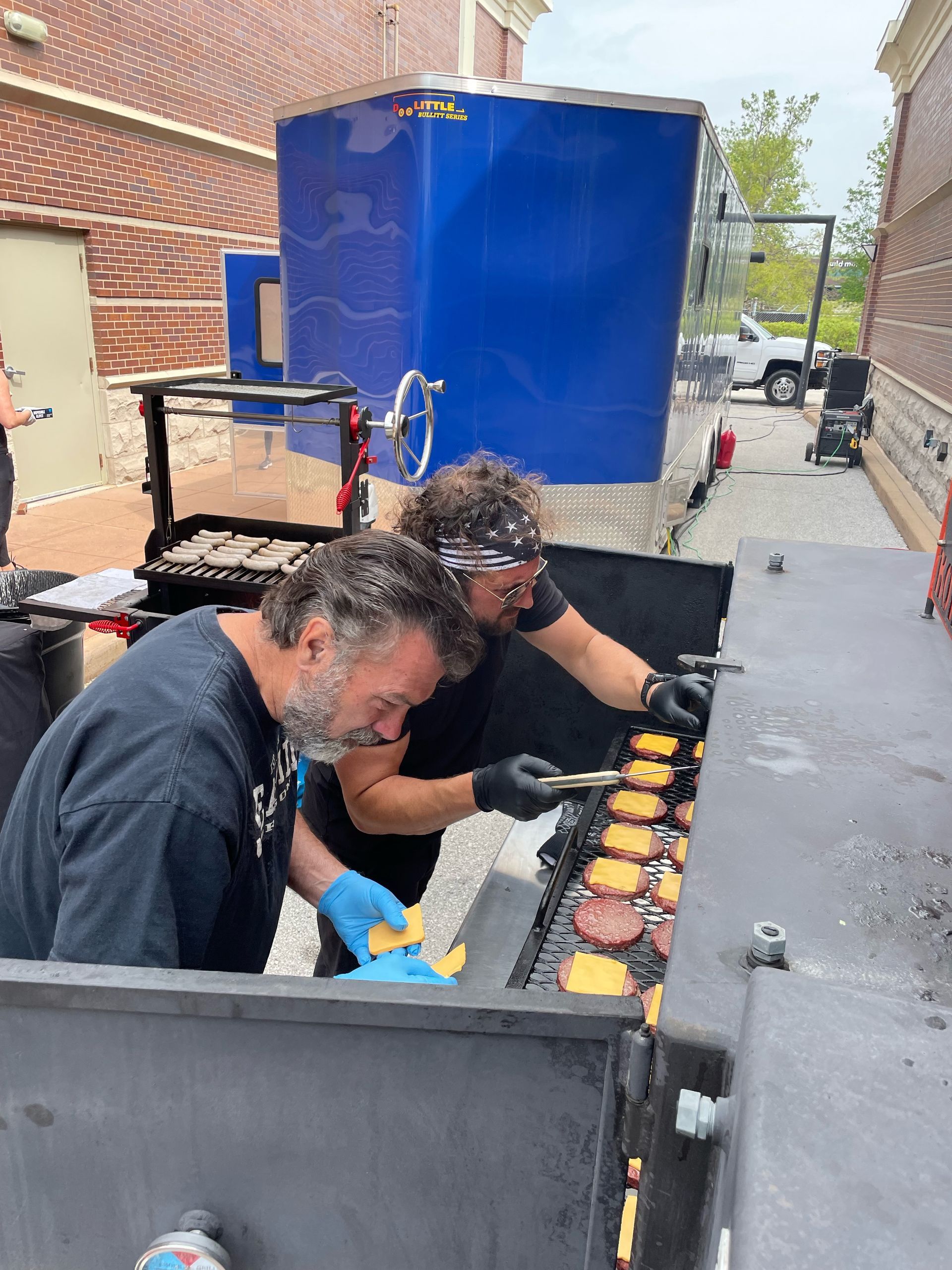 Two men are cooking hamburgers on a grill.