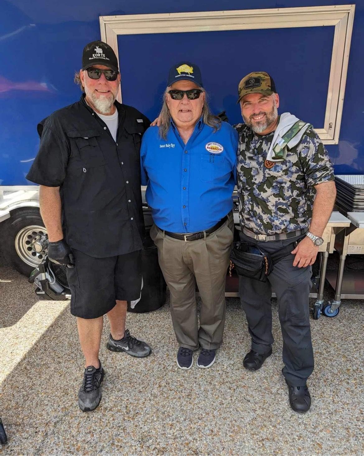 Three men are posing for a picture in front of a blue trailer.
