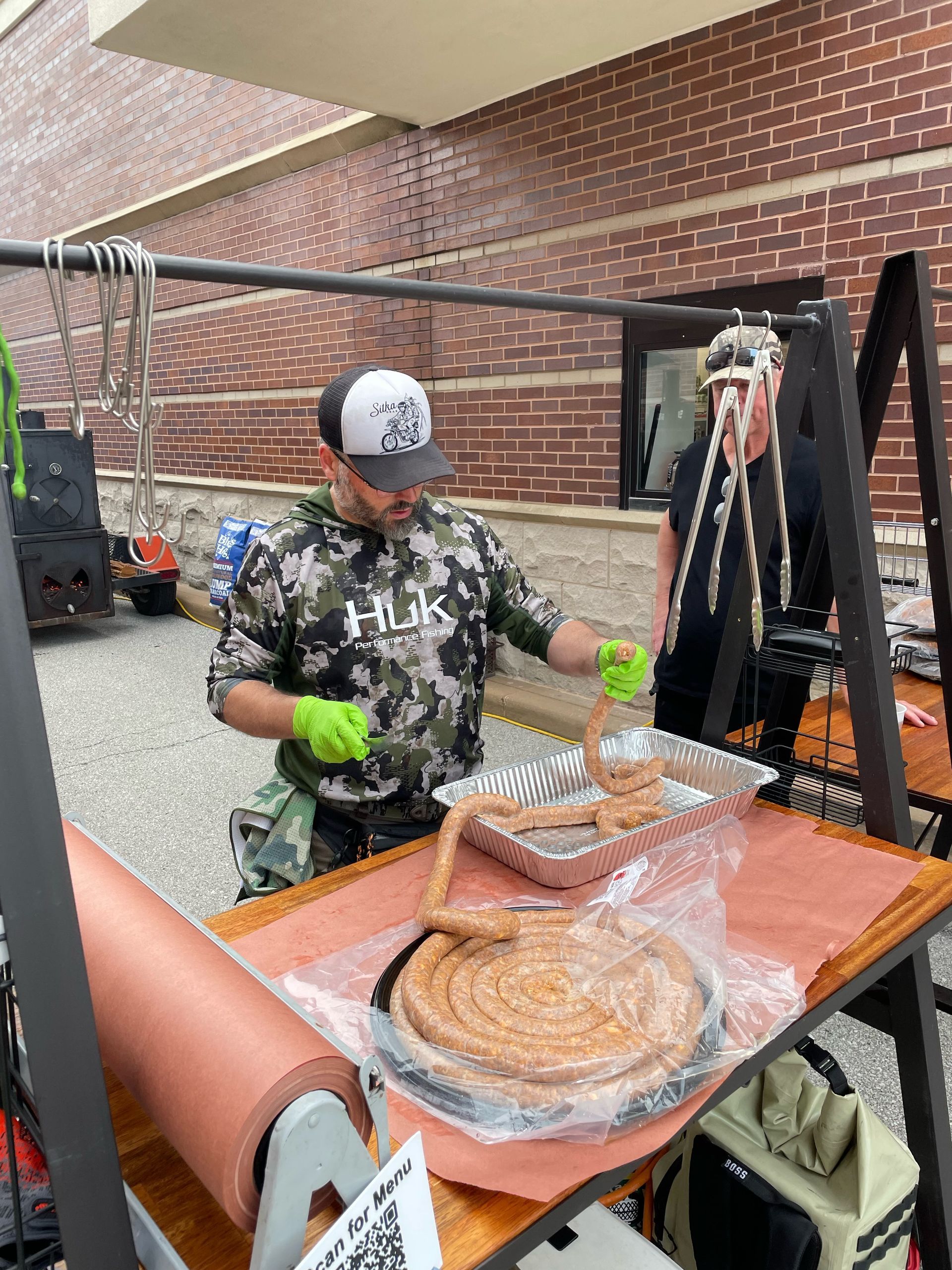 A man is making sausages on a table in front of a brick building.