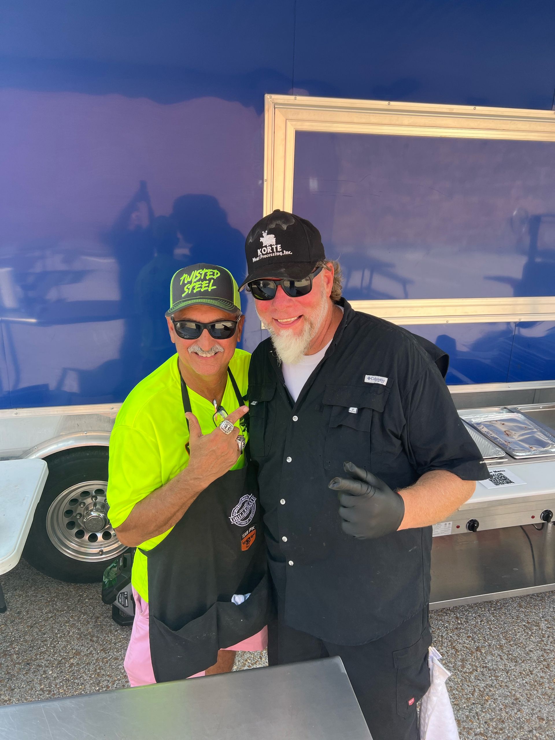 Two men are posing for a picture in front of a blue trailer.