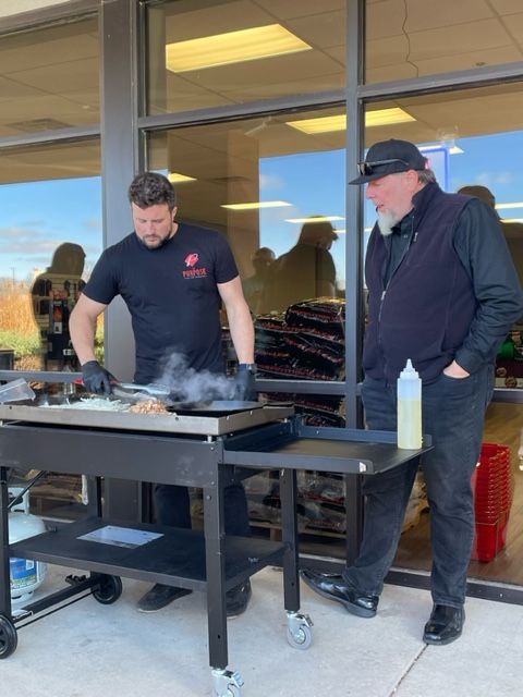 Two men are standing in front of a grill with smoke coming out of it