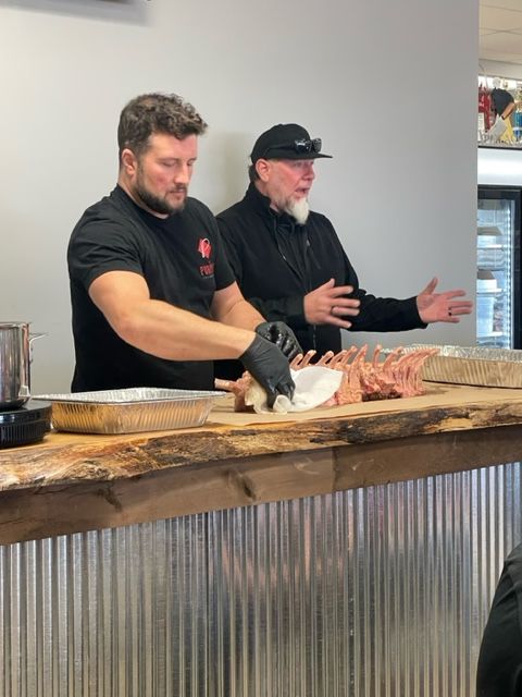Two men are standing at a counter cutting meat