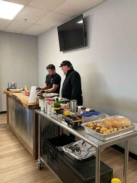 Two men are preparing food in a room with a tv on the wall.