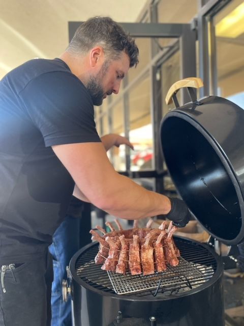 A man in a black shirt is cooking meat on a grill