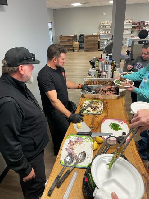 A group of men are standing around a table with food on it.