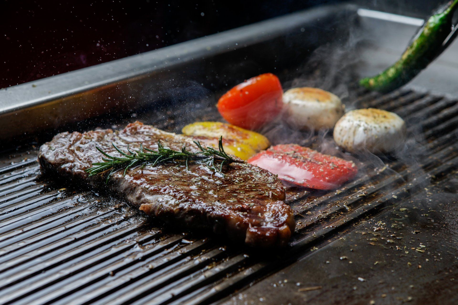 A steak is being cooked on a grill with vegetables.