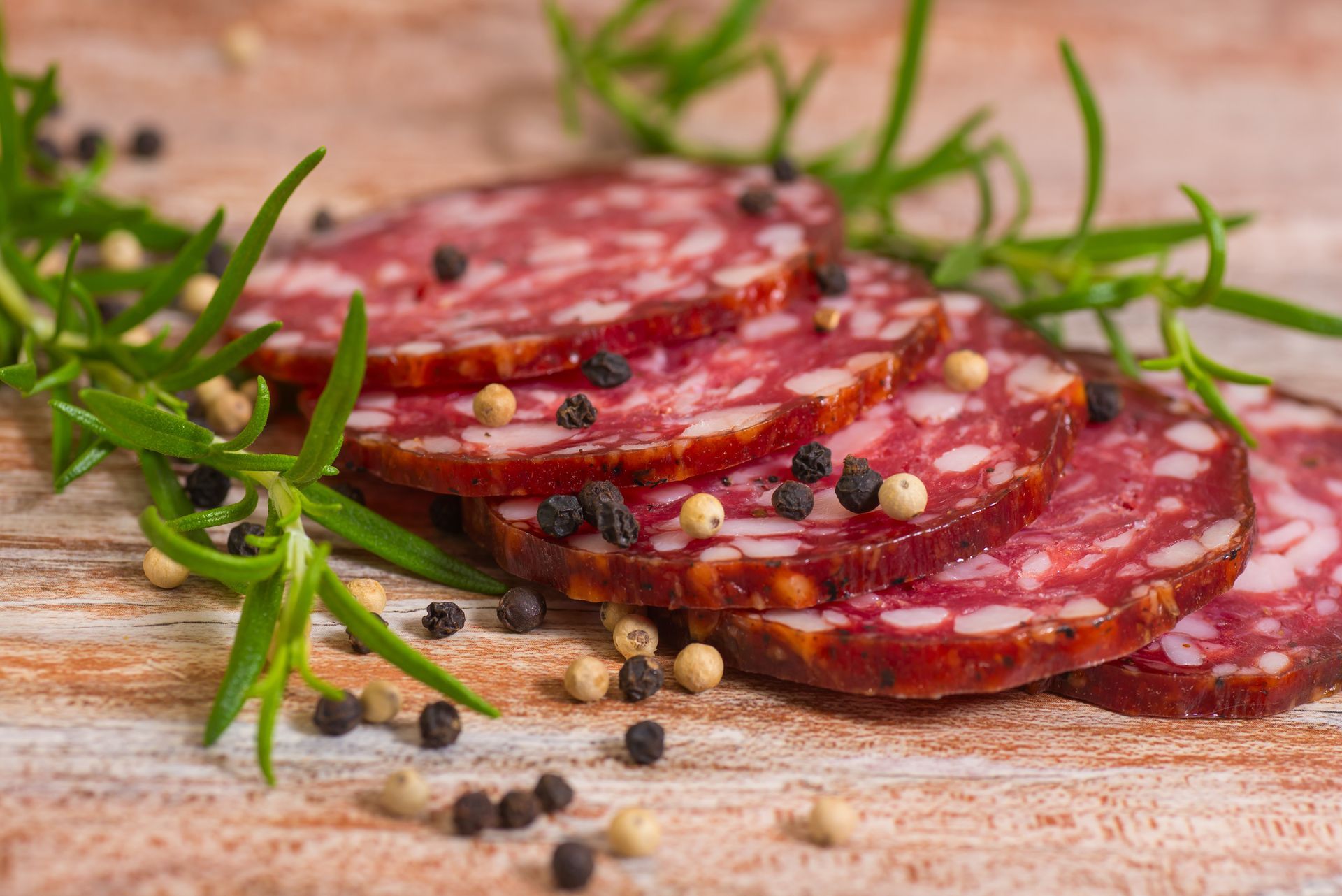A salami is sitting on a wooden cutting board with lettuce and peppers.