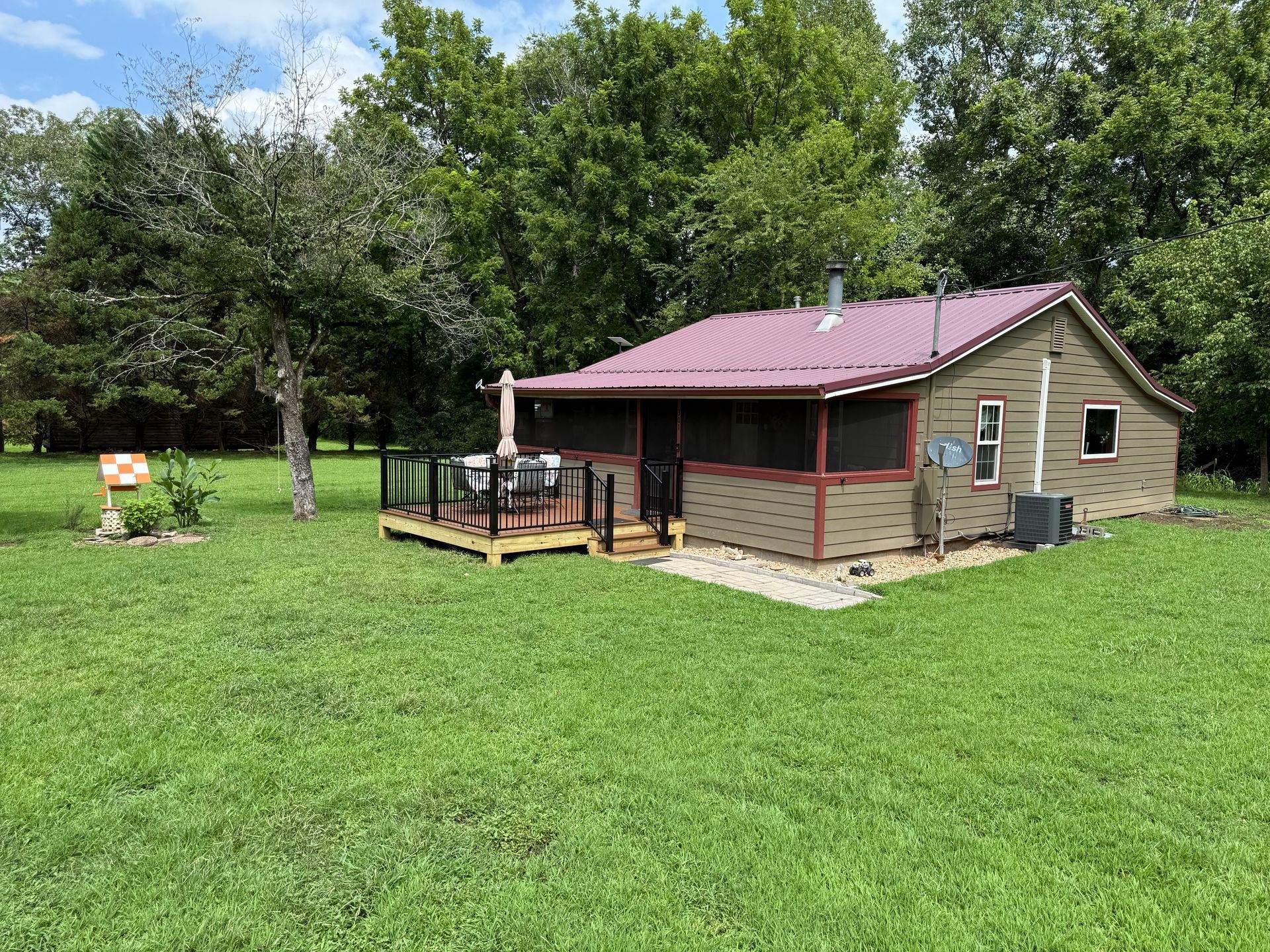 A small green cabin with a red roof and a deck on a grassy lawn.