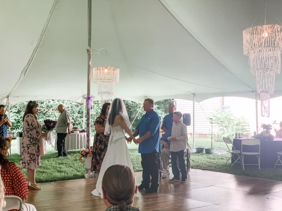 Bride and groom holding hands under a tent, with family watching during outdoor wedding ceremony.