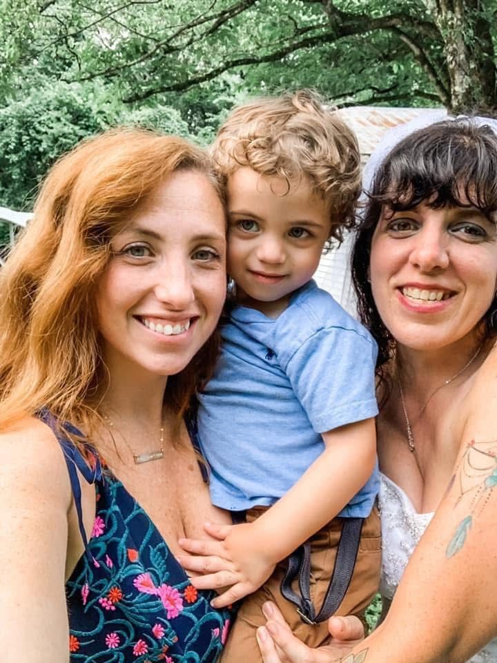 Woman with red hair, a toddler, and a woman with dark hair smiling outside.