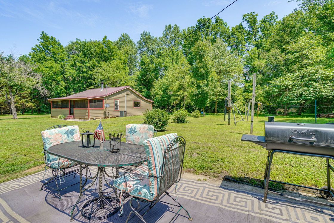 A patio with a table and chairs and a grill in front of a house.
