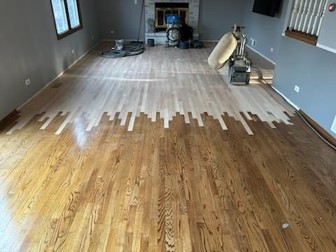 Hardwood floor being refinished, showing a transition from light wood to a stained, darker brown.