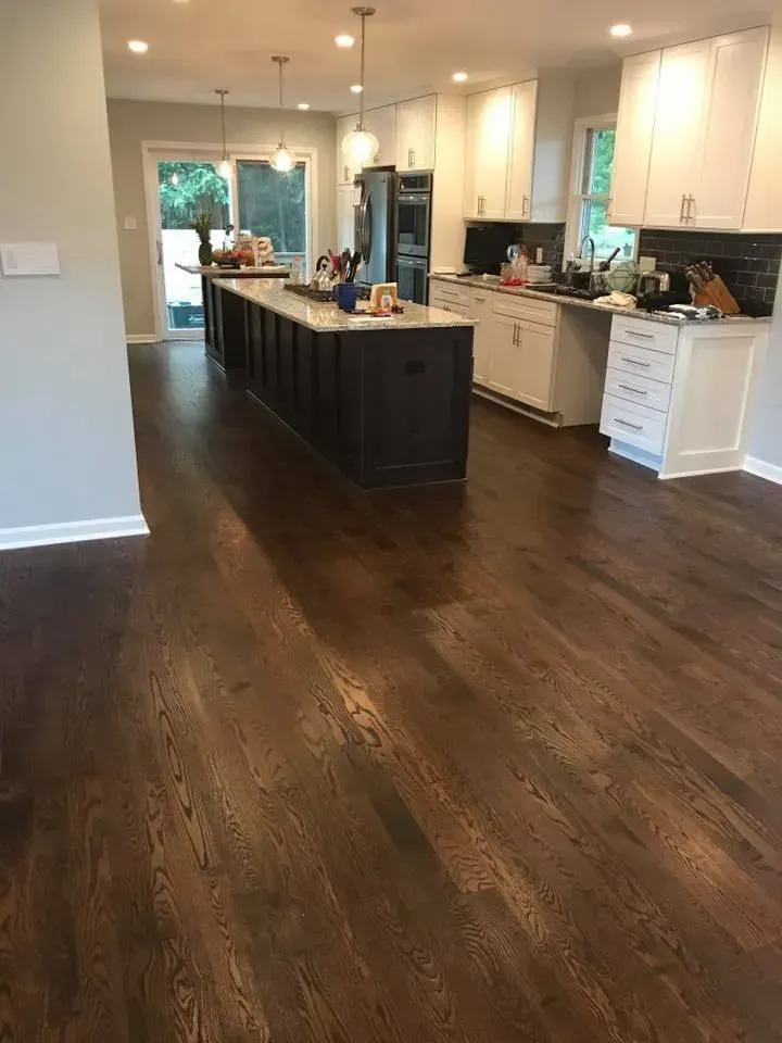 Hardwood floors in a kitchen with a dark island, white cabinets, and a sliding glass door.