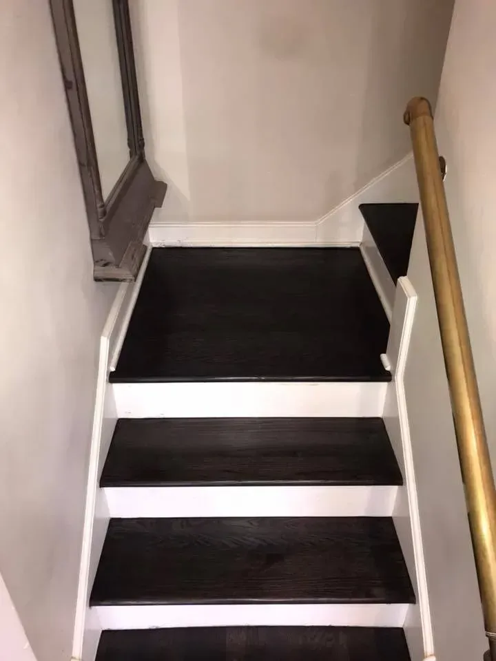 Dark stained wooden stairs with white trim and a gold handrail.