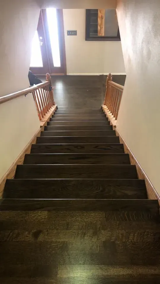 Wooden staircase leading up to a door, with wooden railings and dark hardwood flooring.