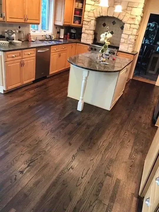 Kitchen with dark wood floors, light wood cabinets, stainless steel appliances, and a granite island.
