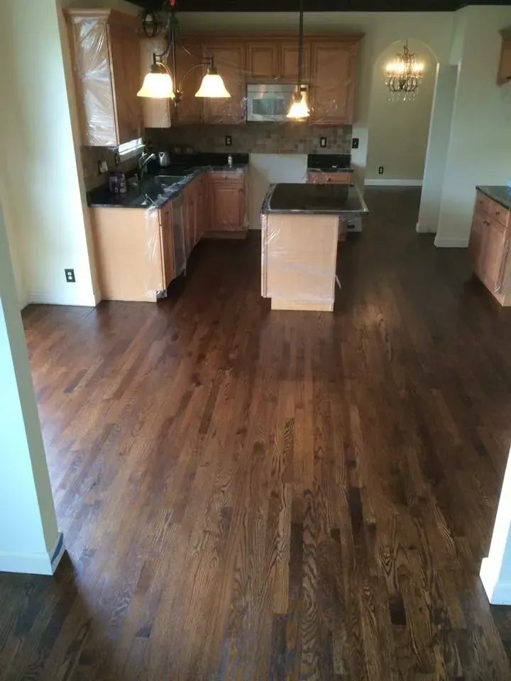 Dark wood floors in a kitchen with light wood cabinets, black countertops, and pendant lights.