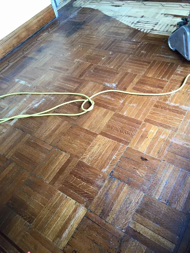 Wood parquet flooring being cleaned with a machine; yellow cord lies across the floor.