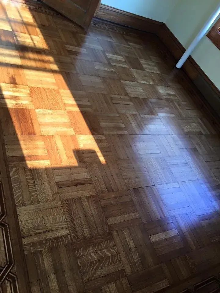 Wooden parquet floor with sunlight and shadows.