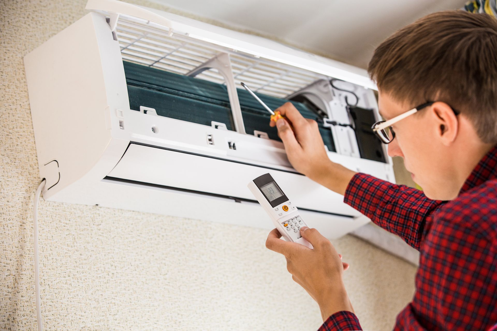 A technician is testing a wall-mounted unit with a remote for a professional AC repair company.