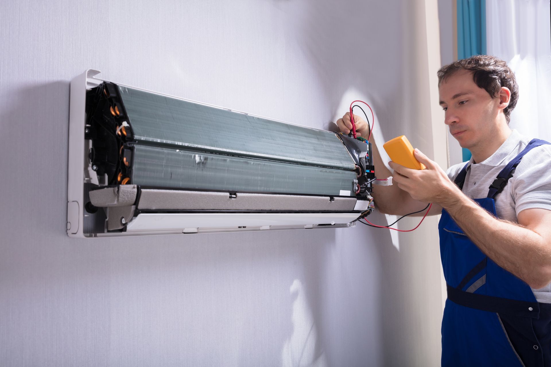 Male AC technician tests an AC unit with a digital multimeter, representing AC repair services.