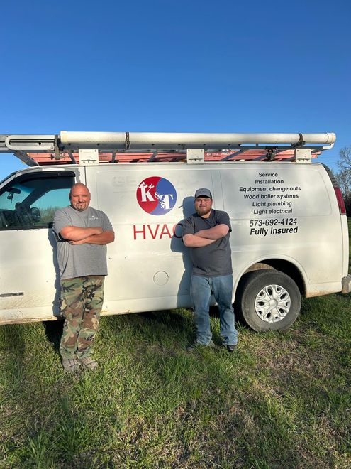 Two men stand in front of a white HVAC van with arms crossed, in a grassy area, under a blue sky.