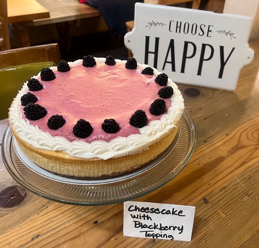 A cheesecake with blackberry topping next to a sign that says choose happy